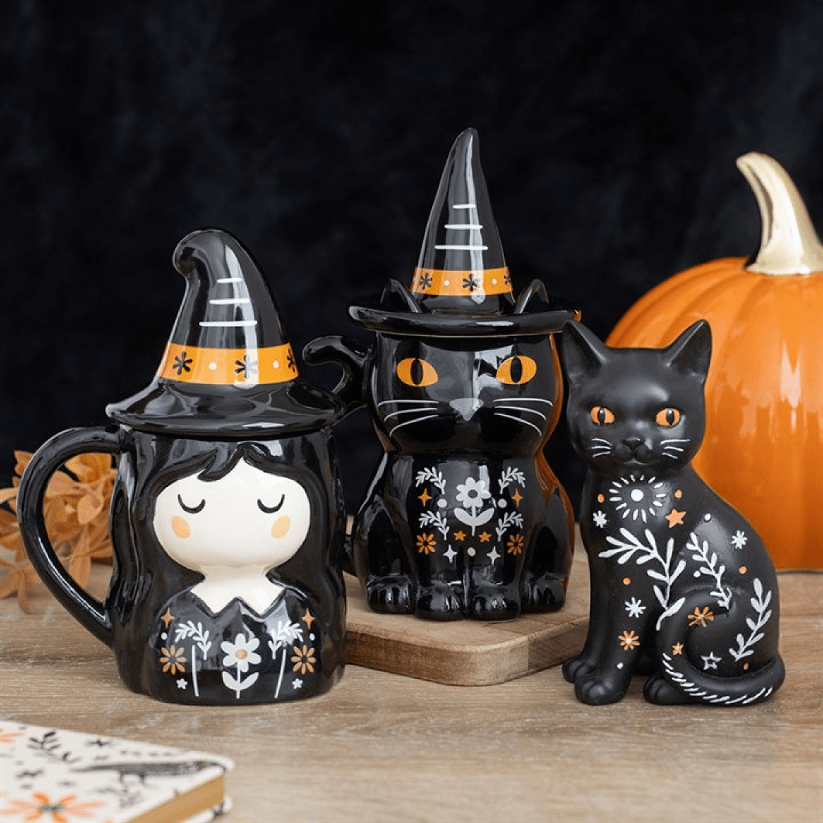 Halloween themed cat ornament and witch mugs on a wooden surface with a pumpkin