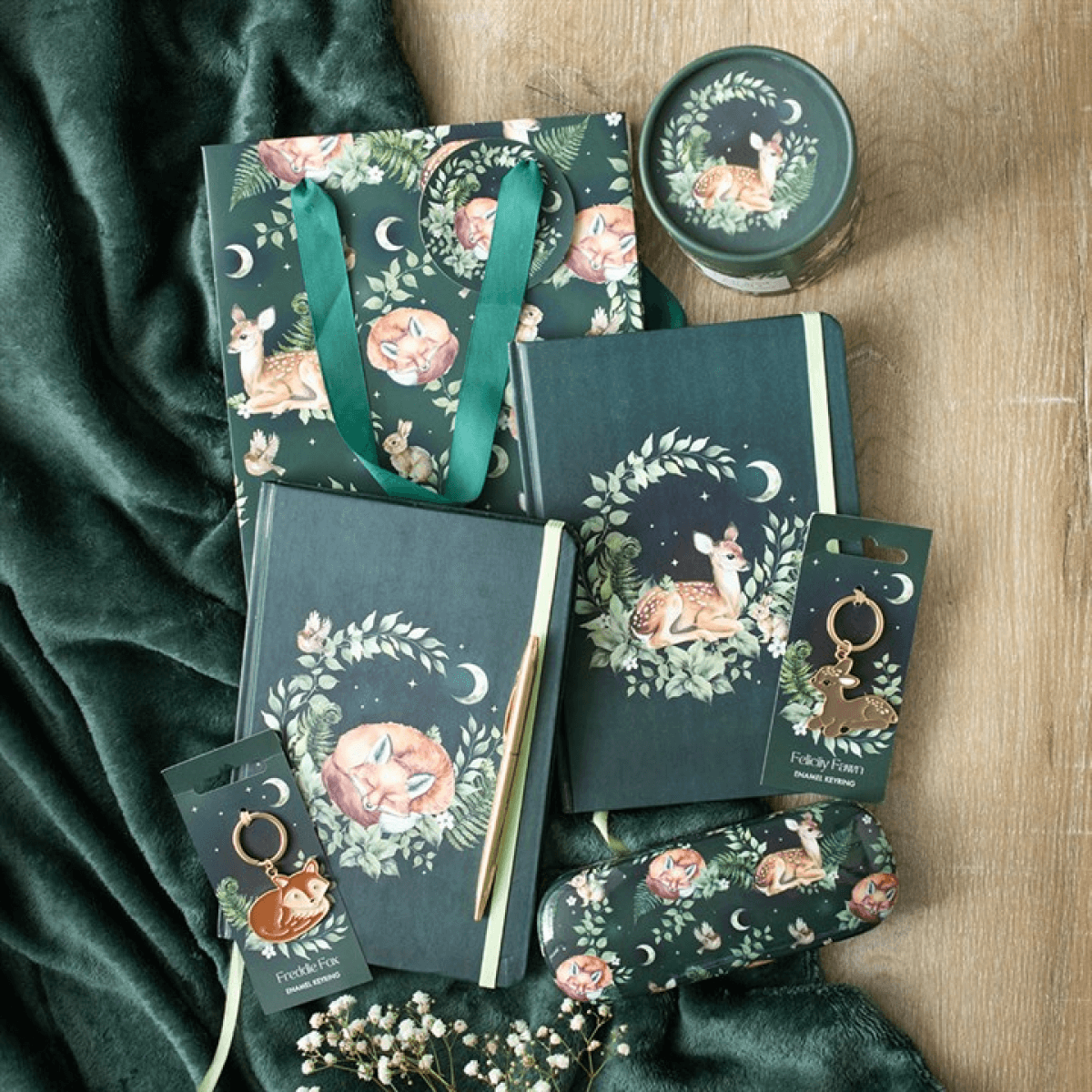 Collection of green-themed products including notebooks, bags, and keychains with nature and animal designs on a wooden surface.
