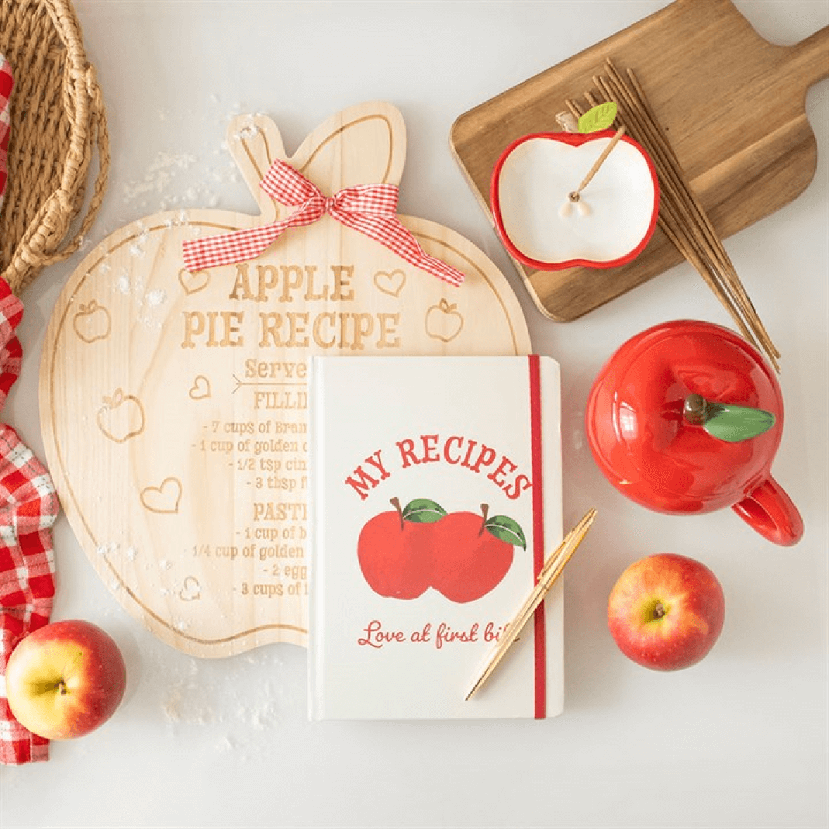 Apple-themed kitchen items including a wooden cutting board, mug, and recipe book on a white surface.