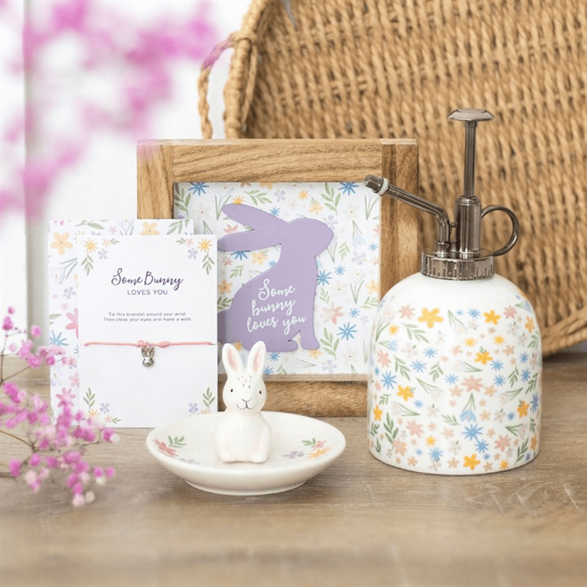 Decorative items including a soap dispenser, rabbit figurine, and cards on a wooden surface with flowers in the background.