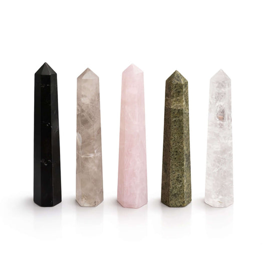 Gemstone obelisks including black, pink, green, and clear quartz points arranged in a row on a white background.