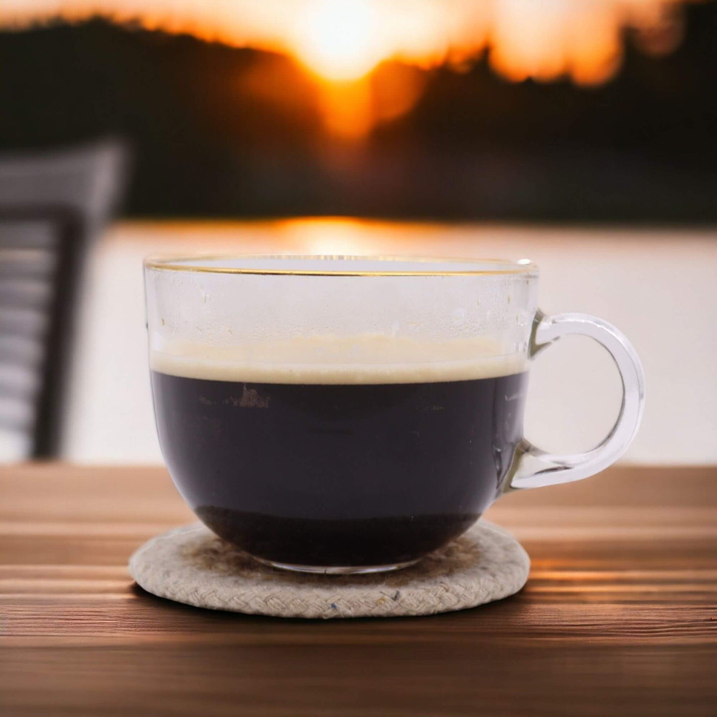 Natural Coaster holding a glass cup of coffee outdoors at sunset on a wooden table.