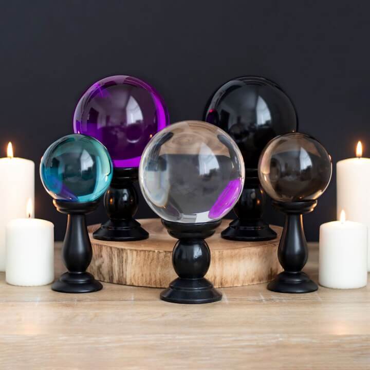 Set of crystal balls on stands with candles around them on a wooden surface.