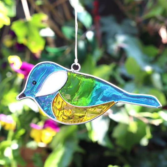 Colorful bird-shaped glass ornament hanging against a green leafy background