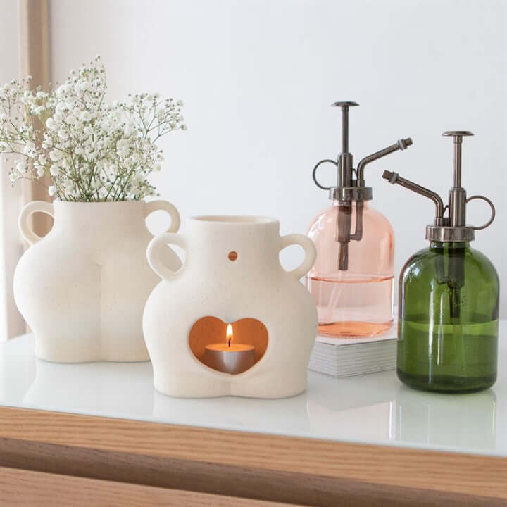 Decorative items including a ceramic vase with a heart-shaped cutout, a white vase with flowers, and glass bottles on a surface.