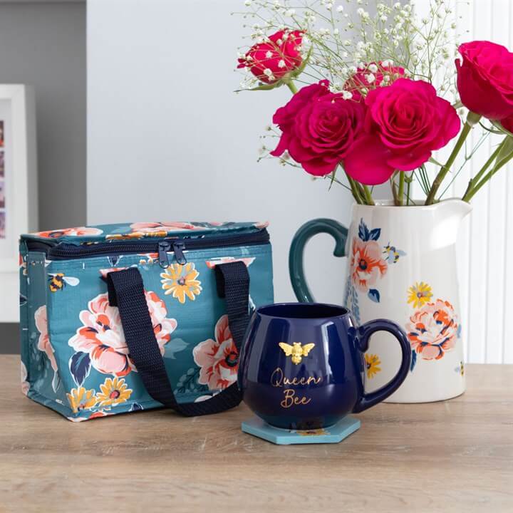 Floral insulated lunch bag, blue mug with 'Queen Bee' text, and floral-patterned pitcher on a wooden surface.