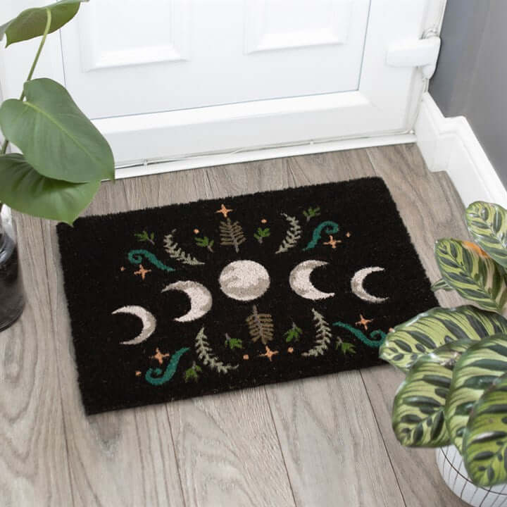 Decorative doormat with moon phases and nature-themed design on a wooden floor.
