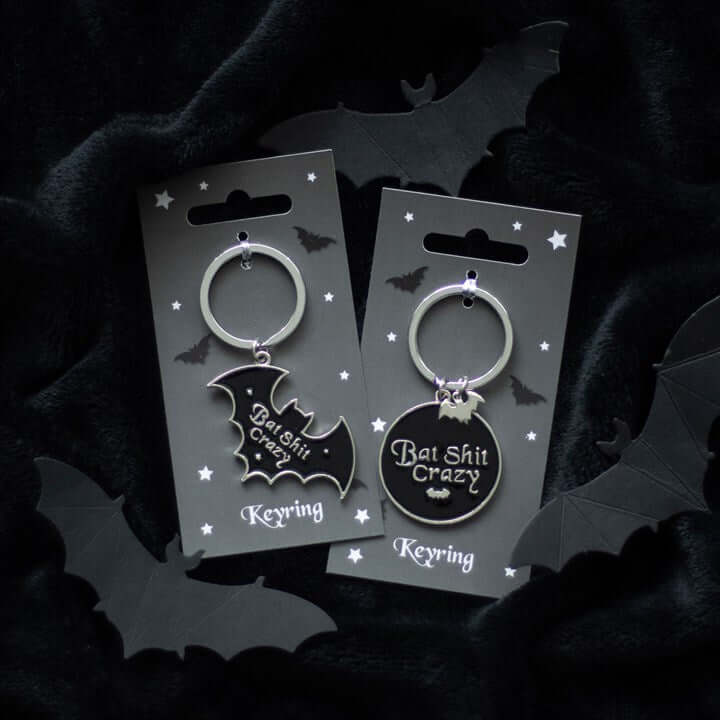 Two keychains on cards with bat designs and text, surrounded by black bats on a dark background.
