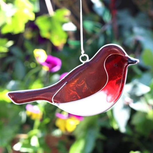 Stained glass bird ornament with a red and white design hanging against a blurred garden background.