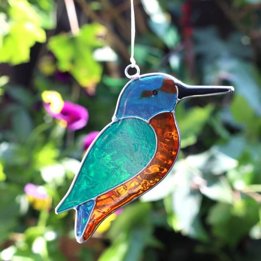 Stained glass kingfisher hanging against a blurred green foliage background