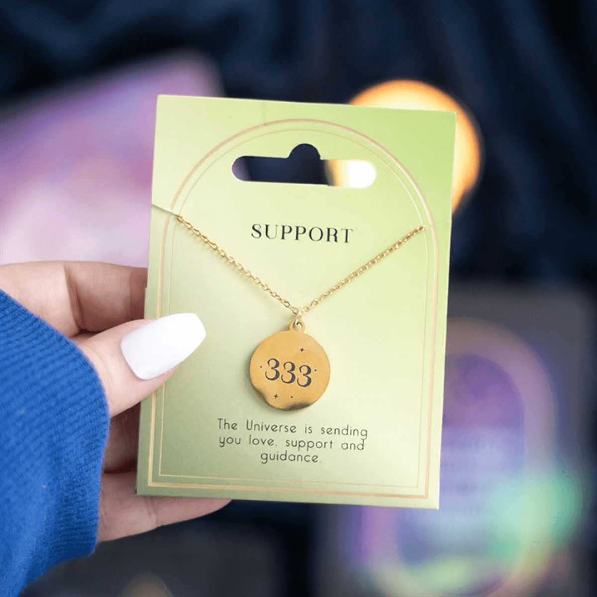 333 Angel Number Support Necklace displayed on a card with a green background and a person's hand holding it.