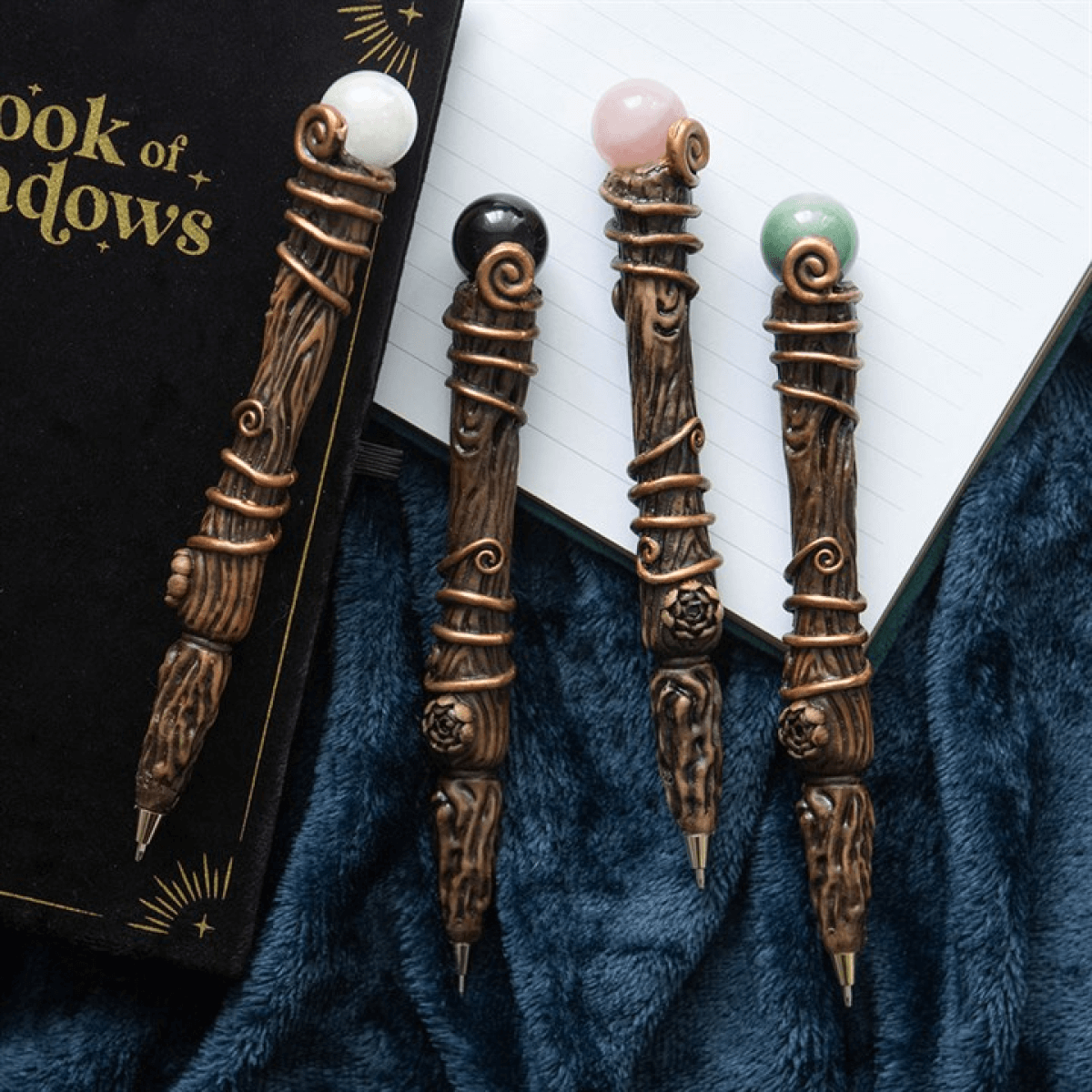 Four ornate pens with gemstones on a blue fabric background