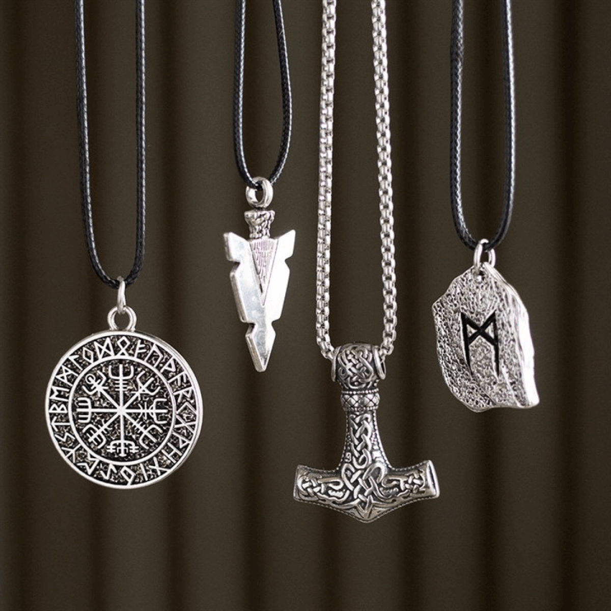 Four silver pendants on black cords against a brown background