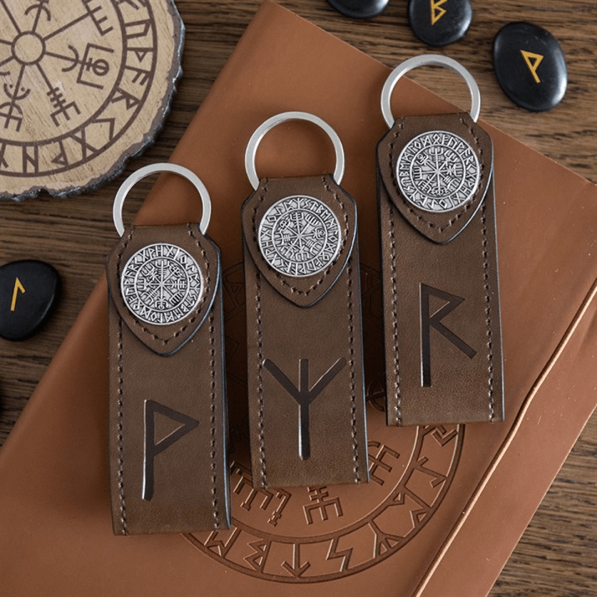 Three brown leather keychains with silverRunes on a wooden surface.