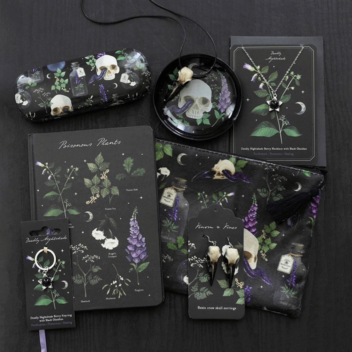 Collection of dark-themed products including a notebook, phone case, and pouches with skull and plant designs on a black background.