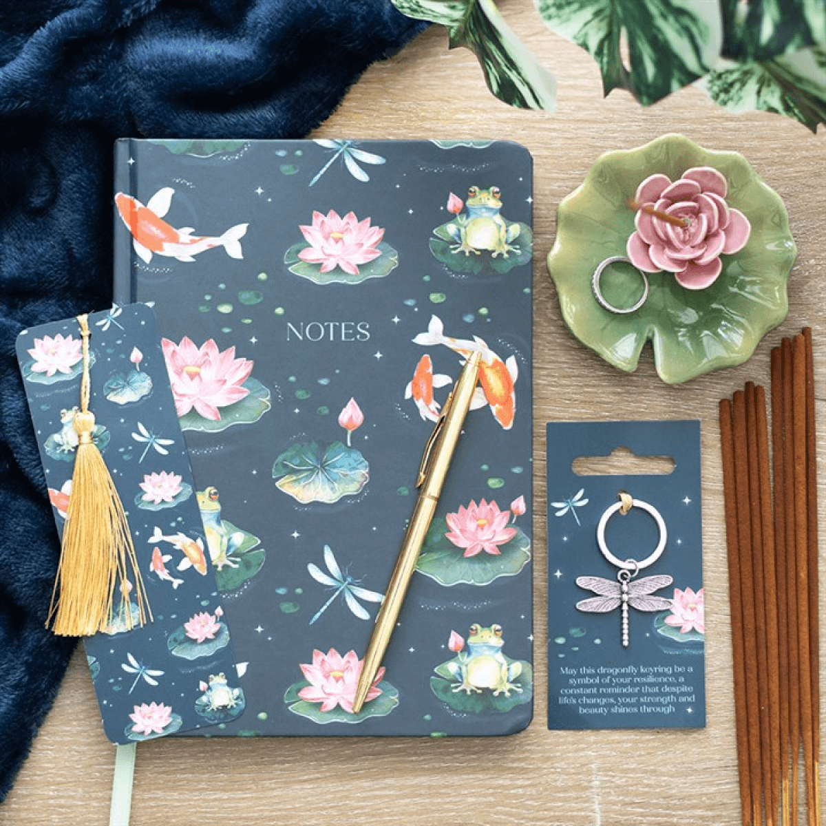 Notebook with nature-themed design, pen, keychain, and decorative items on a wooden surface.