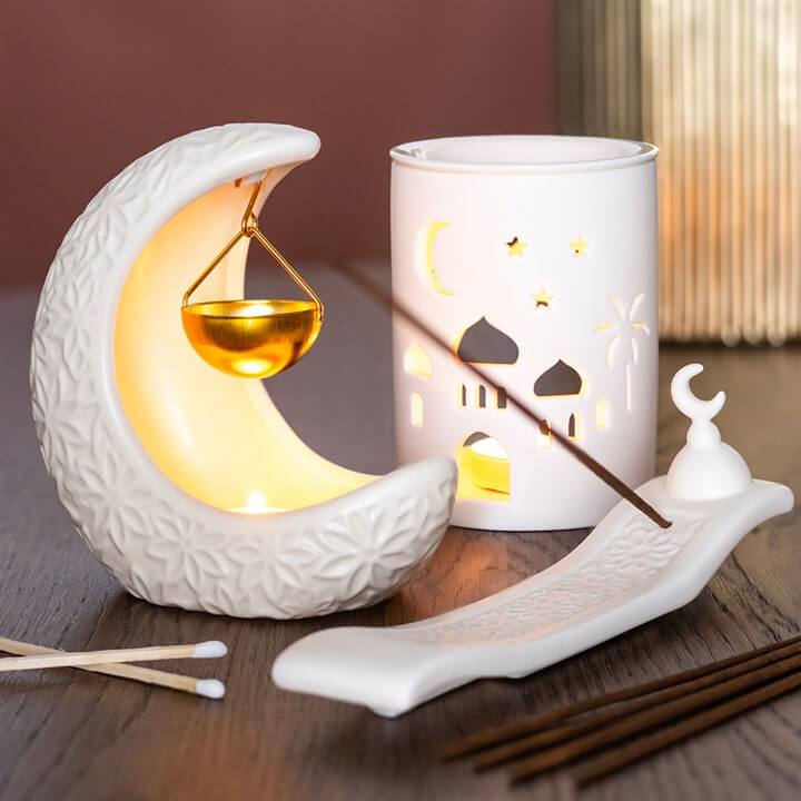 Decorative items including a moon-shaped lamp, lantern with cut-out designs, and incense burner on a wooden surface.