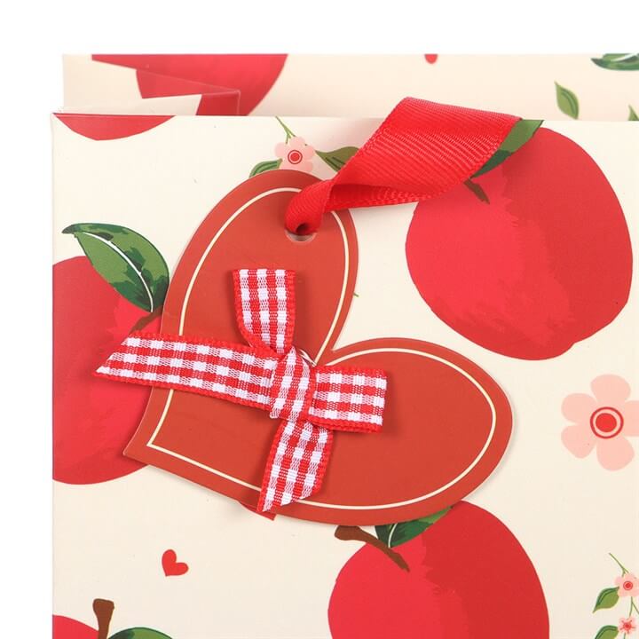Red heart-shaped card with a red ribbon on a background with red apples and green leaves.