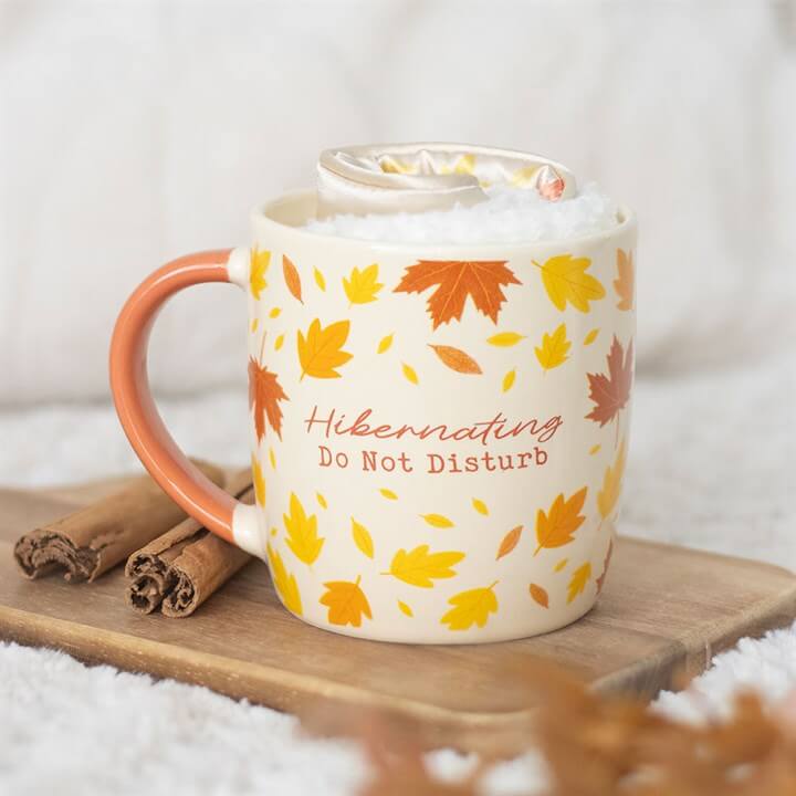 Ceramic mug with autumn leaves design and 'Hibernating Do Not Disturb' text, perfect for cozy evenings with Socks and Eye Mask.