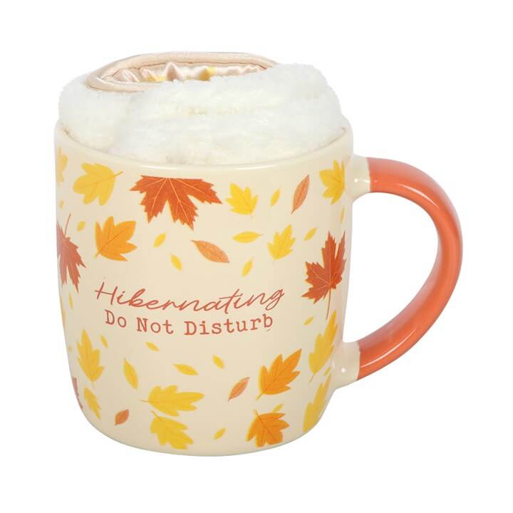 Ceramic mug with autumn leaves design, cozy lid, and text 'Hibernating Do Not Disturb', perfect for relaxation with Socks and Eye Mask.