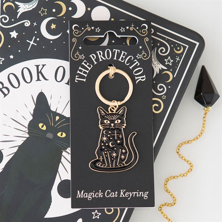 The Protector Magick Black Cat Keyring on a black and gold packaging with mystical designs and a book in the background.