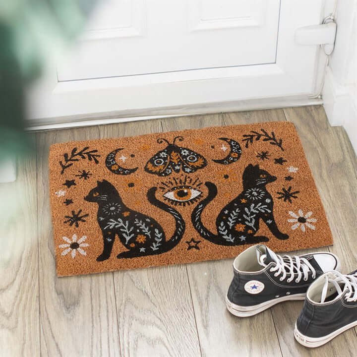 Welcome guests with a touch of mystical charm using the Natural Frightful Folk Cat Doormat. Featuring a bold folk-inspired design, this eye-catching mat showcases two black cats, celestial moons, and a central all-seeing eye—perfect for adding a hint of s