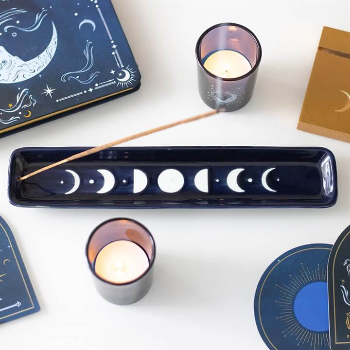 Blue Moon Phase Ceramic Incense Ash Catcher with candles and celestial artwork around it.