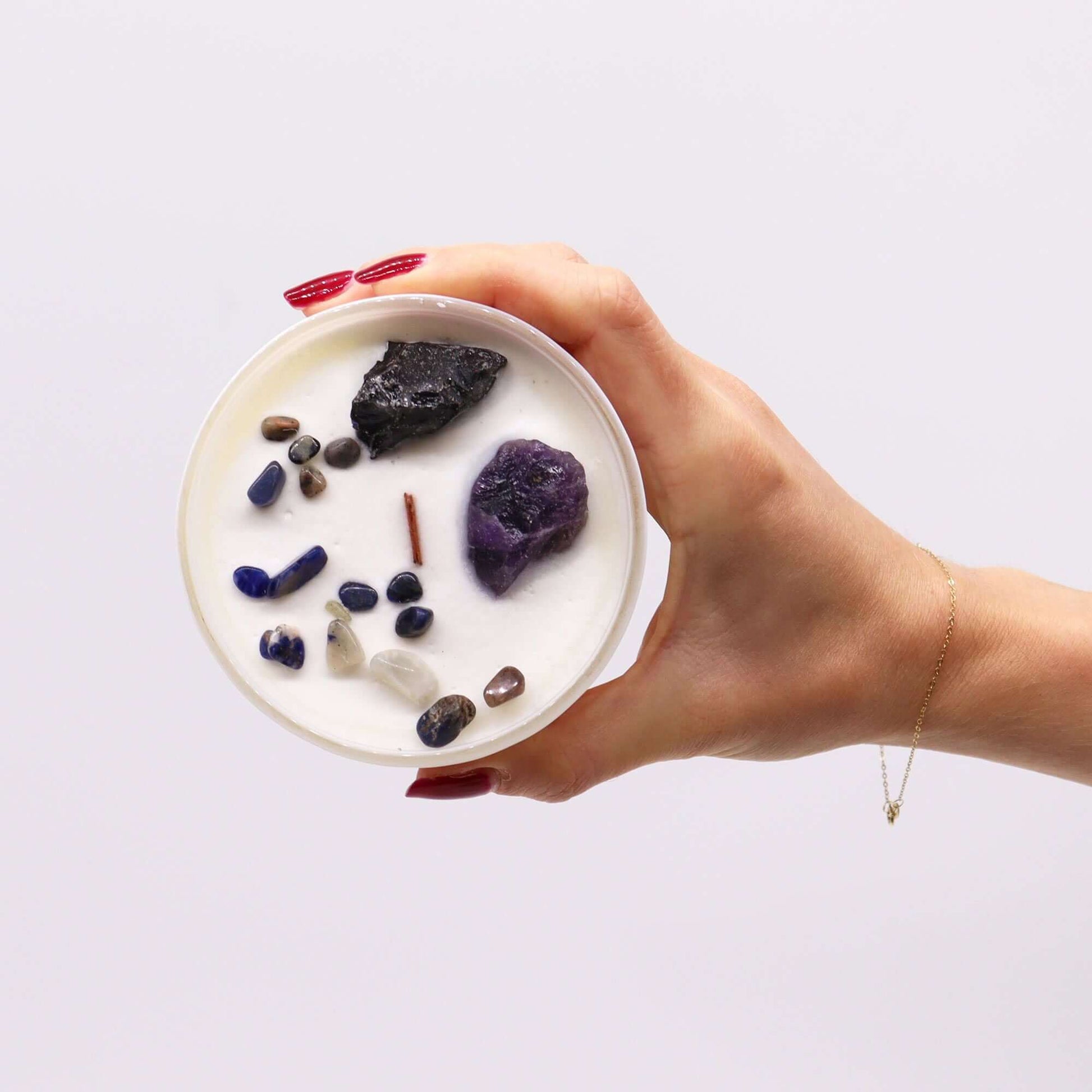 Hand holding a circular candle with various crystals, symbolizing the Solar Plexus Chakra.