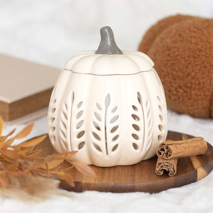 Cream Leaf Cut Out Pumpkin Oil Burner and Wax Warmer on a wooden tray with cinnamon sticks, perfect for autumn decor.