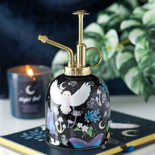 Decorative mist sprayer with artistic design on a surface with a candle and plant in the background.