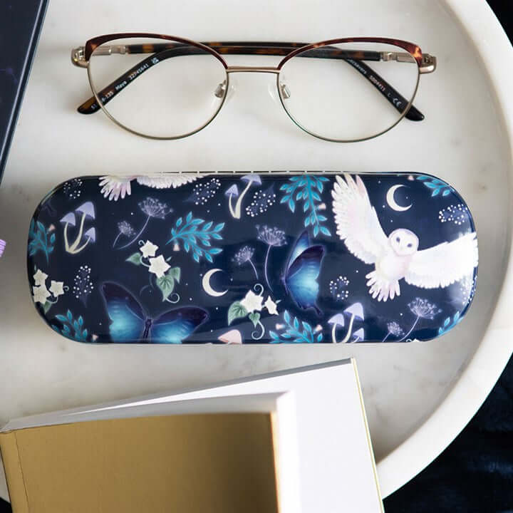 Eyeglasses on a white surface with a decorative case featuring nature-themed designs.