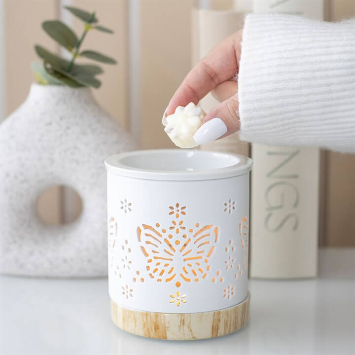 Matte Ceramic Butterfly Oil Burner with a hand adding wax, featuring butterfly cut-outs for soft illumination.