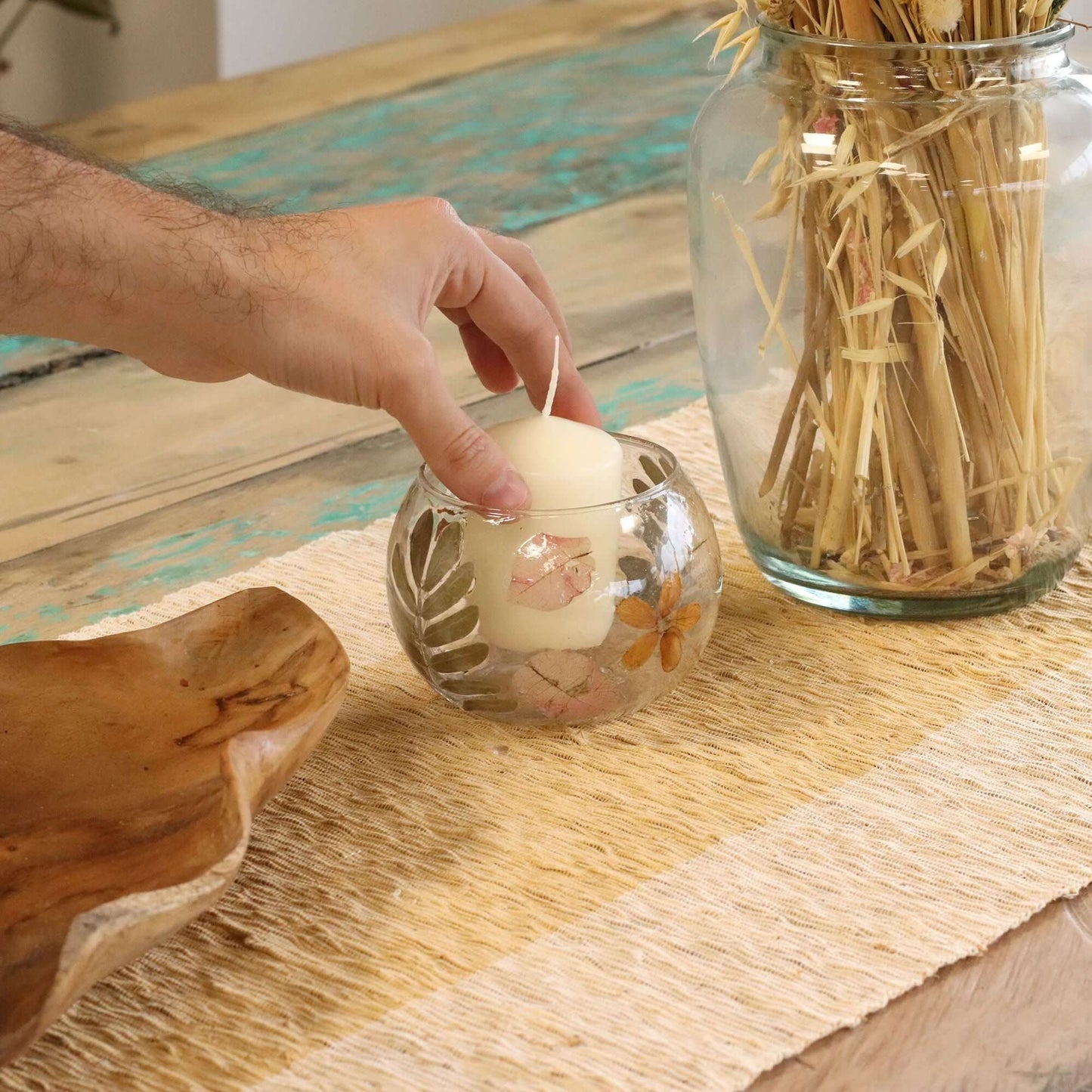 Hand placing a candle in a Natural Floral Glass Bowl Candle Holder on a table with a rustic décor.