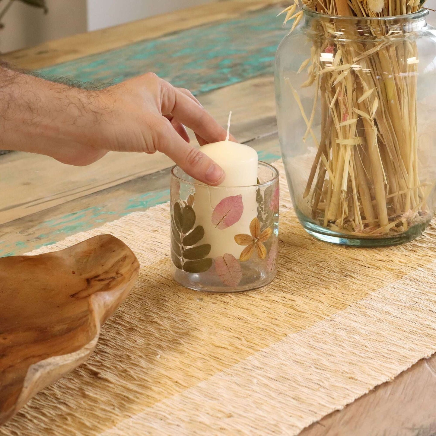 Hand placing a pillar candle in a Natural Floral Candle Holder surrounded by nature-inspired decor.