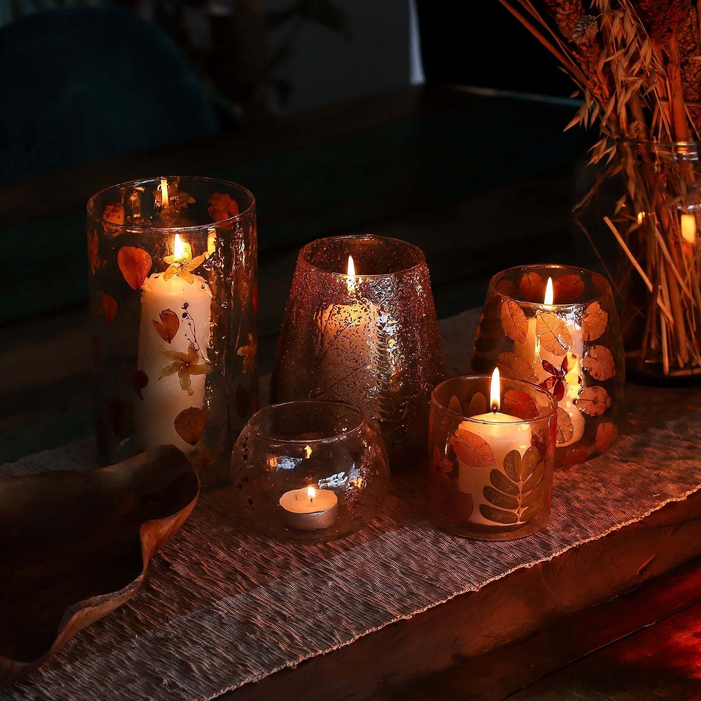 Natural Floral Candle Holder collection with lit candles, showcasing pressed leaves and blossoms in a cozy setting.