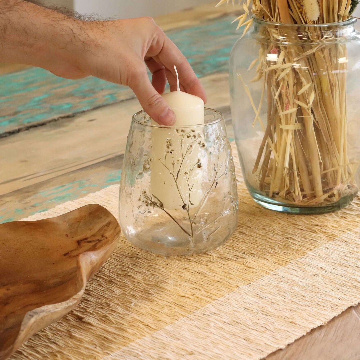 Hand placing a candle in a Natural Floral Glass vase candle holder with preserved flowers on a rustic table.