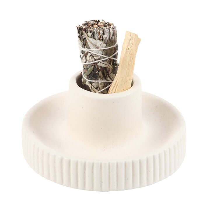 White ceramic incense holder with dried herbs and a wooden stick on a white background