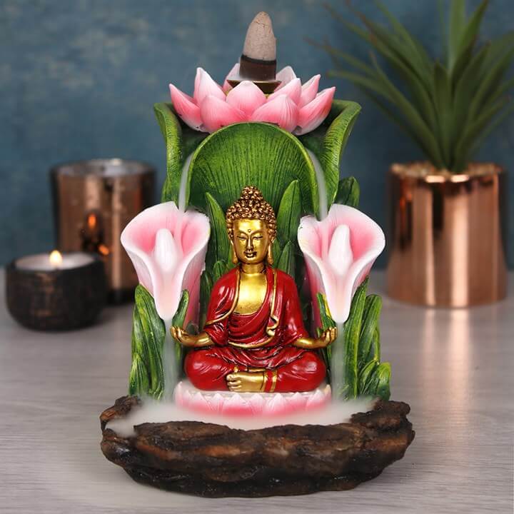 Decorative statue of a seated Buddha figure with pink flowers and green leaves on a reflective surface.