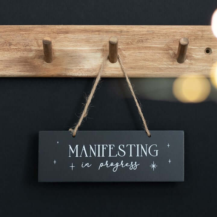 Hanging Sign that says 'Manifesting in progress' on a wooden hook for meditation and spellcasting.