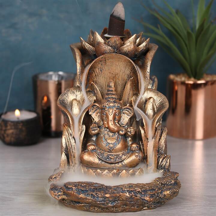 Bronze deity statue with incense burner on a table with candles and plants in the background.