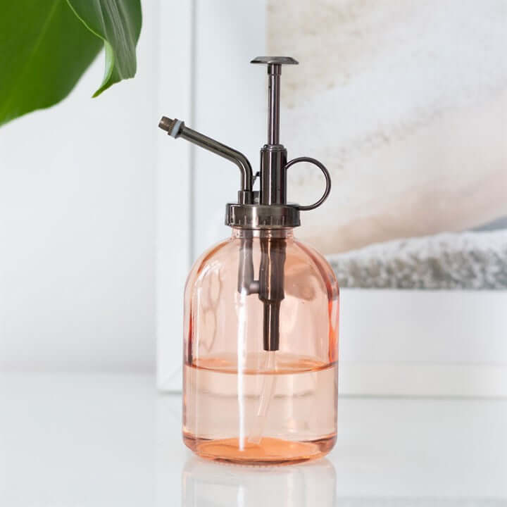 Pink glass spray bottle with metal nozzle on a white surface