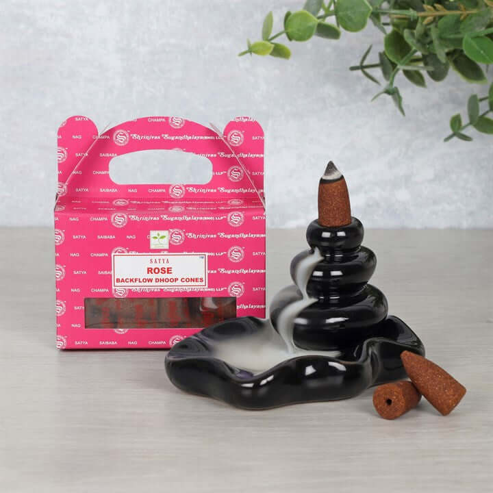 Black incense burner with cones and pink packaging on a light gray surface.