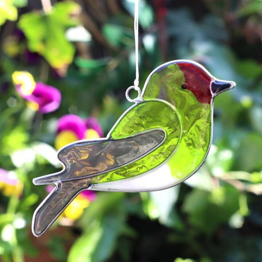 Stained glass bird ornament hanging against a garden background with flowers and greenery.