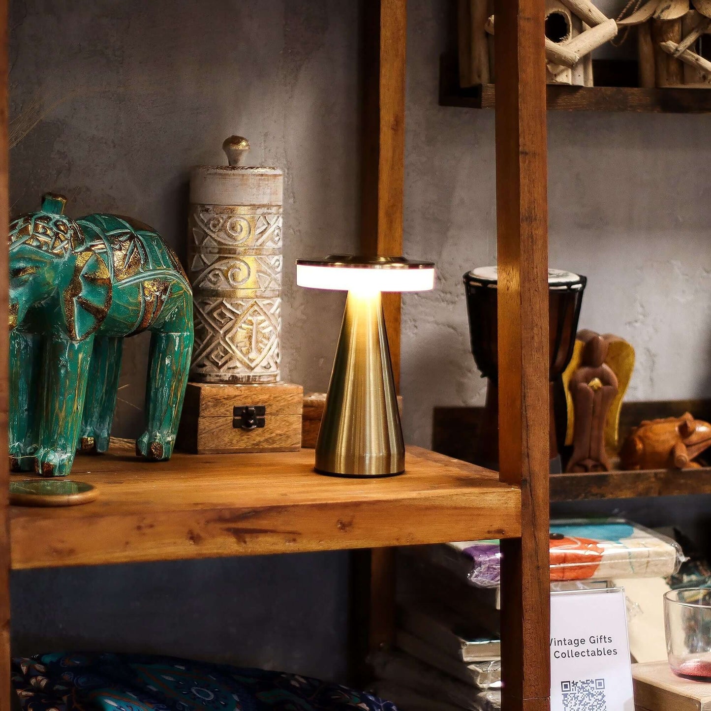 Touch Lamp Tall on a wooden shelf beside decorative items, showcasing its modern design and copper finish.