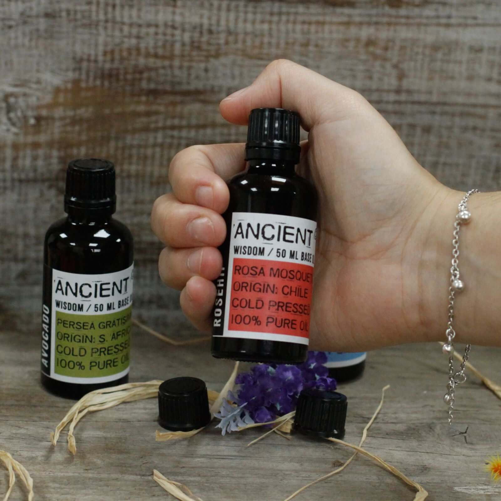 A hand holding a bottle of Apricot Kernel Oil - 50ml with labels on a rustic wooden background.