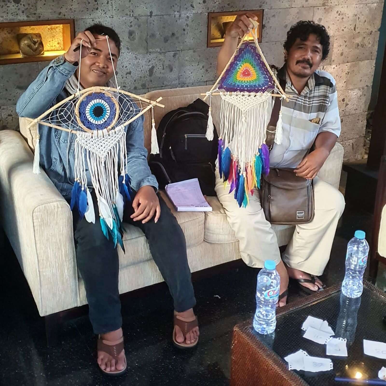 Two individuals displaying handcrafted Protection Dream Catchers featuring Evil Eye designs in blue, white, and grey.
