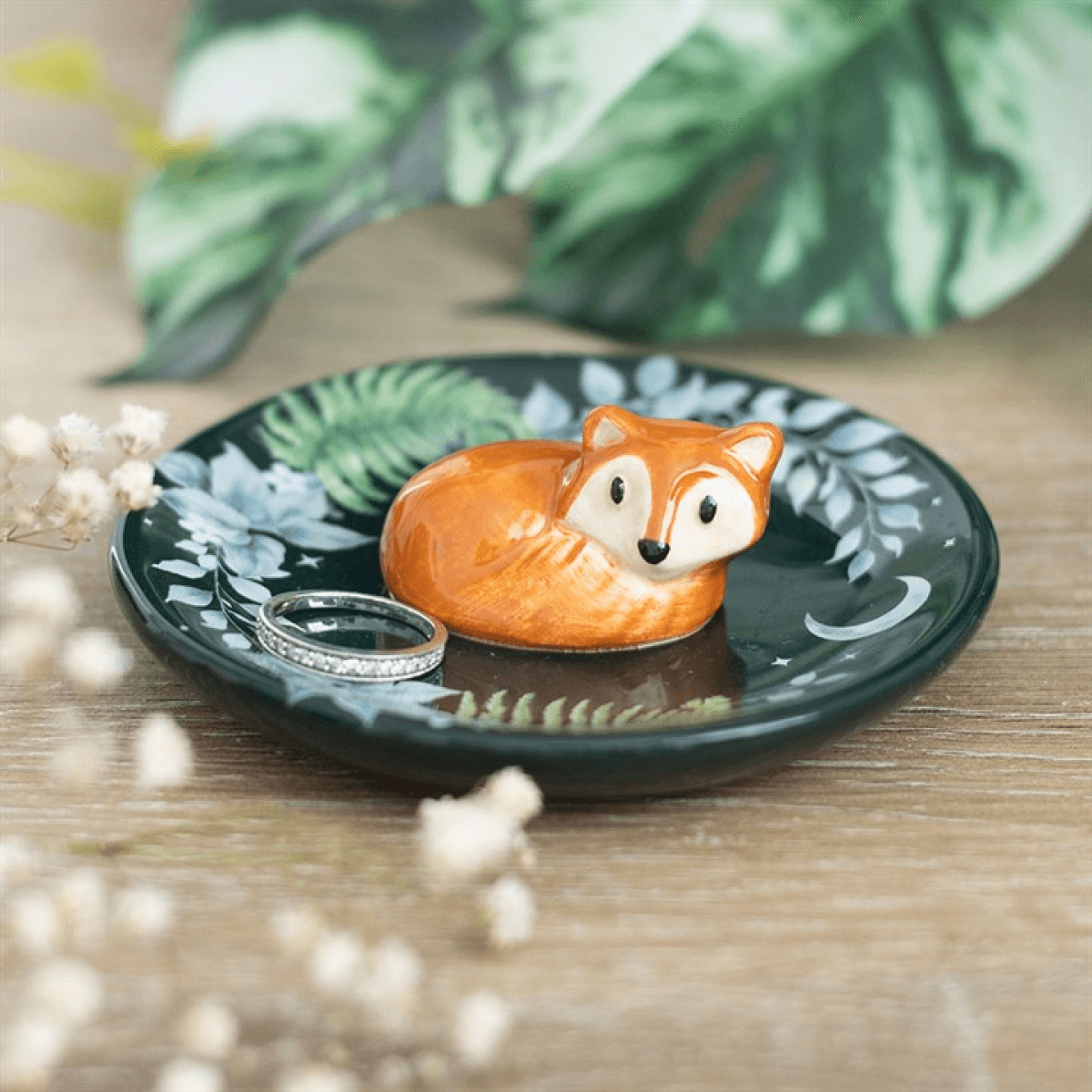 Decorative dish with a fox figurine and ring on a wooden surface with green leaves in the background