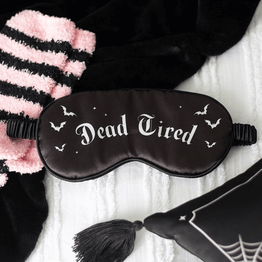 Black sleep mask with 'Dead Tired' text and bat designs on a white blanket.
