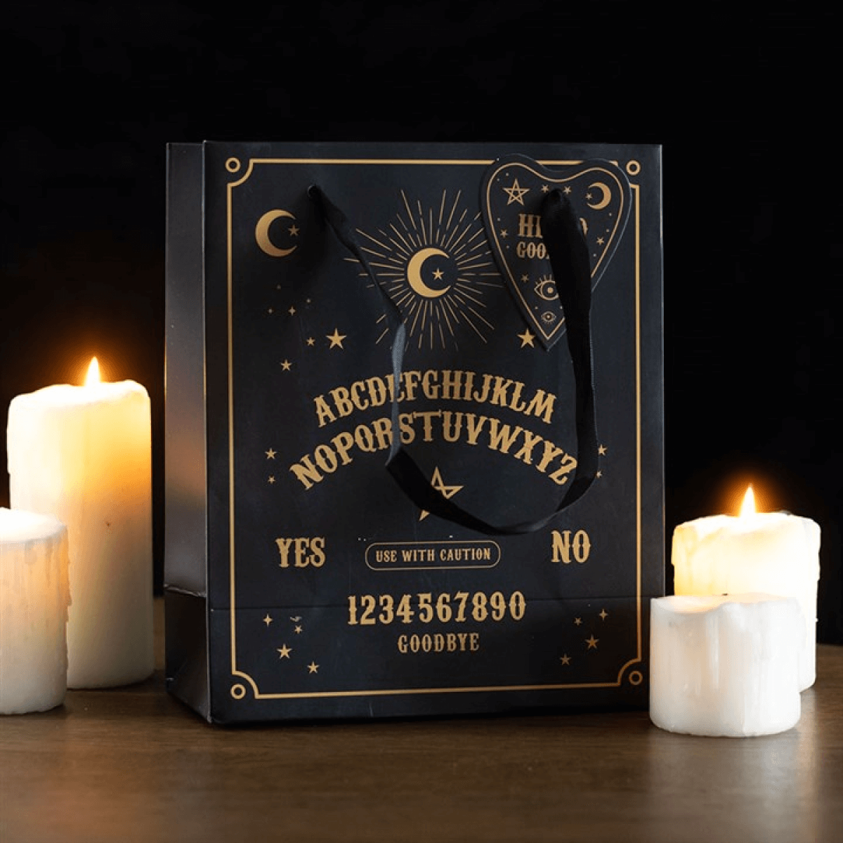 Black gift bag with gold text and symbols, surrounded by candles on a dark background