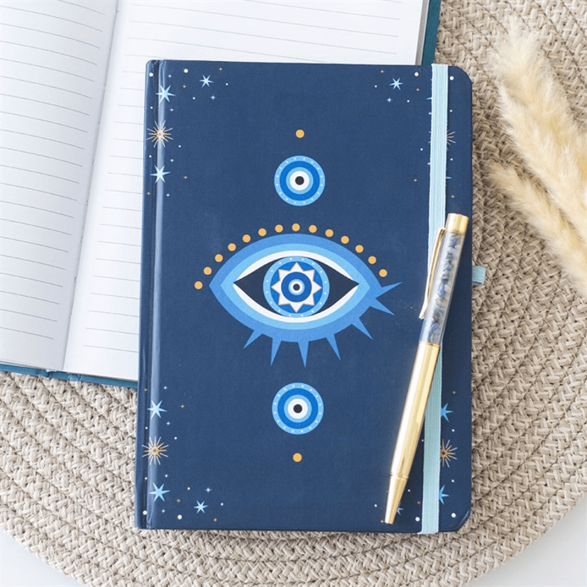 Notebook with a blue cover featuring an eye design, next to a gold pen on a textured surface.